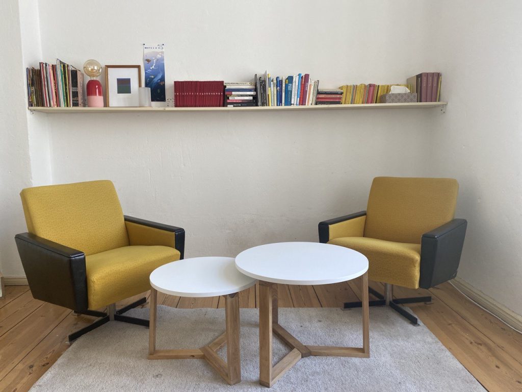 Auf dem Foto ist ein Systemischer Coaching und Beratungsraum in Berlin zu sehen. Darin befinden sich zwei gelbe Sessel und zwei weiße Tische.